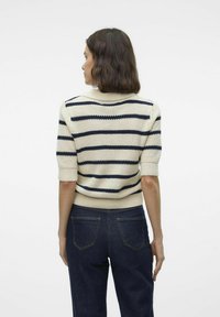 Gebreide trui met korte mouwen, voorzien van horizontale crèmekleurige en marineblauwe strepen, textuurstof en een geribbelde halslijn. Draagt met donkere jeans.
