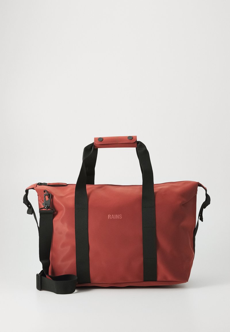 Un sac de sport rouge avec des sangles noires, doté d'une fermeture éclair et d'une bandoulière. Le nom de la marque "RAINS" est visible à l'avant.
