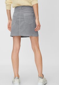 Falda de mezclilla gris con un dobladillo deshilachado, dos bolsillos traseros y un diseño ajustado, combinada con zapatillas de color claro.