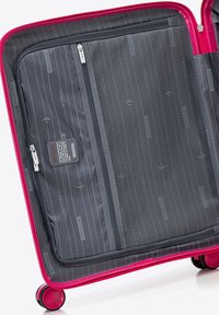 Interno della valigia rigida rosa con scomparti zip grigi, tasca in rete, tessuto texturizzato e fodera personalizzata con motivi di aerei stampati.