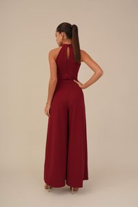 Combinaison bordeaux avec un col haut, un détail de dos en trou de serrure et une coupe à jambes larges. Fabriquée en tissu lisse, avec une construction sans coutures.