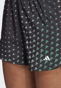 Svarta shorts med ett geometriskt mönster av vita och gröna trianglar. Tillverkade av mjukt tyg med resår i midjan och en liten logotyp.