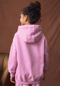 Felpa con cappuccio rosa realizzata in tessuto morbido con vestibilità comoda, dotata di cappuccio con coulisse e polsini a coste. Texture liscia, design semplice.