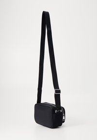 Borsa a tracolla nera con forma rettangolare, realizzata in tessuto morbido, dotata di chiusura zip e tracolla regolabile, arricchita da dettagli in metallo argentato.