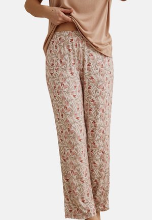 Femme portant un pantalon ample taille haute avec un motif floral feuillu beige, marron et rose, associé à un haut beige légèrement relevé.