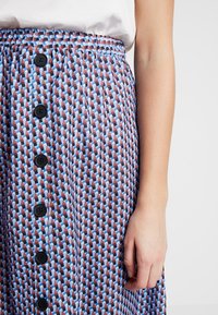 Gonna con bottoni caratterizzata da un motivo geometrico in blu, marrone e rosso. Vita elasticizzata con bottoni neri sul davanti. Texture liscia.