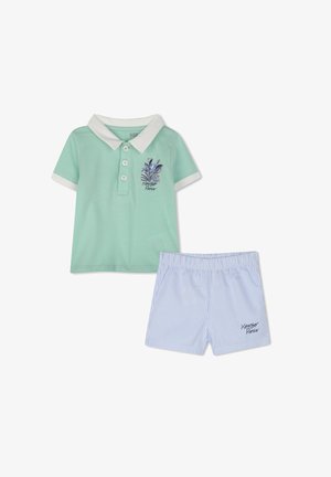 Groene polo met een witte kraag, voorzien van blauwe bloemenborduursels. Gecombineerd met blauw-wit gestreepte shorts met een elastische tailleband.