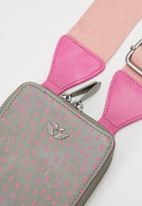 Szara prostokątna torba w różowe kropki, z metalowymi elementami i kontrastującymi różowymi paskami. Posiada mały srebrny emblemat w formie skrzydeł.