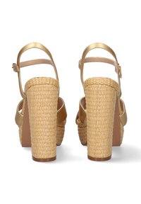 Sandalias de cuña con tacón de paja trenzada, correas de cuero dorado, hebilla ajustable en el tobillo y una suela marrón lisa.