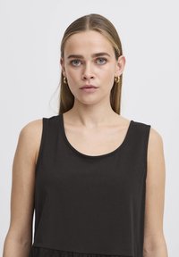 Top nero senza maniche con scollatura tonda, realizzato in un tessuto morbido. Presenta una vestibilità rilassata e un design a strati sull'orlo.
