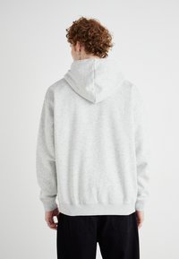 Haut à capuche gris clair avec une texture douce, doté d'une grande capuche et de poignets et d'un ourlet côtelés. La vue arrière montre une coupe ample et décontractée.