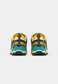 Chaussures de trail, présentant un design multicolore avec des accents jaunes, violets, noirs et teal. Semelle robuste pour une meilleure adhérence.