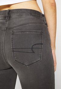 Jean de mezclilla gris con un diseño ajustado, que cuenta con un bolsillo trasero con un detalle de costura negra en contraste y un parche de cuero con marca.