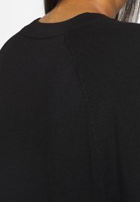 Zwarte katoenen sweatshirt met een ronde halslijn en zichtbare naaddetails bij de schouders, die een zachte, gestructureerde stof laat zien.