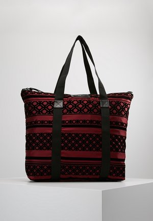 Bolsa tote con estampado rojo y negro, con correas verticales negras y cierre de cremallera, exhibida sobre un pedestal blanco con un fondo liso.