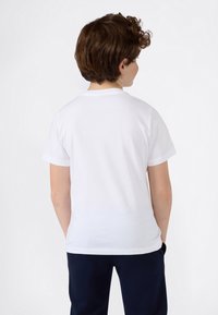 Biała bawełniana koszulka, krótki rękaw, okrągły dekolt, gładka tekstura, noszona z ciemnymi spodniami, widziana z tyłu. Minimalistyczny design.