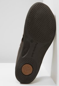 Brown rubber shoe sole featuring a textured grip pattern and embossed branding. Circular accent near the heel adds detail.