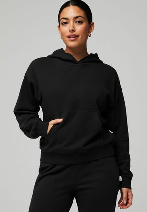 Sweatshirt à capuche noir en tissu doux, doté d'une poche kangourou et de poignets côtelés ; coupe décontractée et design minimaliste.