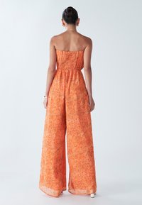 Oranje bloemenjumpsuit met een strapless, gerimpelde bovenkant en wijde broekspijpen. De stof is doorschijnend met een gestructureerd patroon.