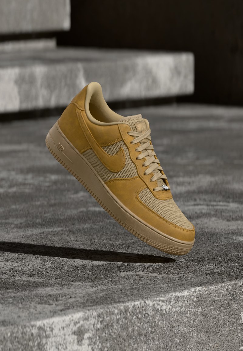 Baskets Nike Air Force 1 beige et marron clair flottant au-dessus d'une surface en béton avec des marches en pierre en arrière-plan.