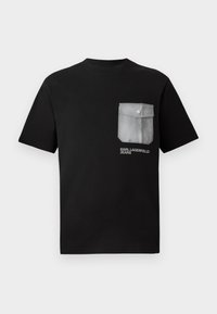 Juodas medvilninis marškinėliai trumpomis rankovėmis, su dideliu pilku kišeniu kairėje krūtinės pusėje ir baltais užrašais "KARL LAGERFELD JEANS."
