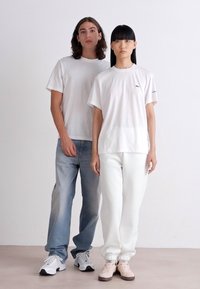 Camisetas blancas, jeans de color azul claro y pantalones de chándal blancos, con un modelo en zapatillas rosas. Textura suave, corte casual, diseño minimalista.