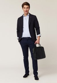 Crna kožna aktovka s dva ručka, slim dizajn. Model nosi marin blue sako, prugastu košulju i marin blue hlače, uz tamne tenisice.