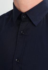 Navy blue button-up shirt featuring a smooth fabric, pointed collar, and plastic buttons. Visible stitching along the placket.
