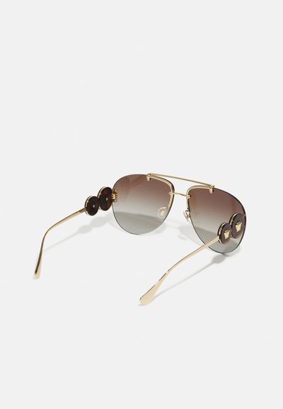 Gold-toned aviator sunglasses with gradient brown lenses and round dark accents on the frame. Features slim, curved temples.