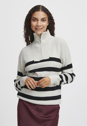 Pull rayé crème avec de larges bandes noires horizontales, doté d'un col haut et d'une fermeture éclair quart. Texture douce avec une coupe décontractée.
