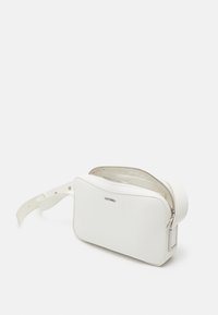 Bílá kožená taška přes rameno Calvin Klein s texturou, metalickým logem, otevřená hlavní přihrádka na zip a nastavitelný pásek na bílém pozadí.