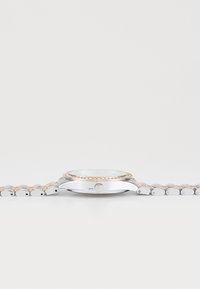 Montre argentée avec une lunette à accent doré, cadran rond et bracelet à maillons métalliques. Présente une couronne simple et un verre transparent.
