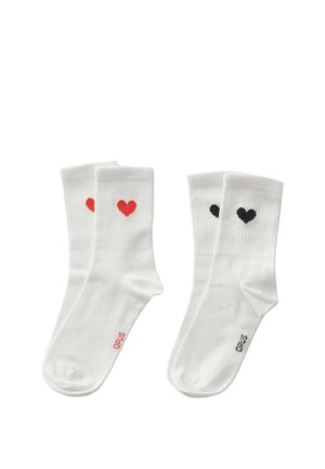 Deux paires de chaussettes blanches de type crew, l'une avec des cœurs rouges et un texte rouge "OPUS", l'autre avec des cœurs noirs et un texte noir "OPUS" près des orteils.