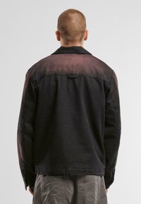 Svart denimjakke med gradientfade fra mørkt til lyst ved skuldrene, med en klassisk krage og knappelukking.