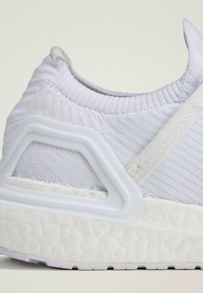 Hvit atletisk sneakers med strikket overdelen, teksturert stoff og en distinkt gjennomsiktig hæl motvekt med en polstret såle.
