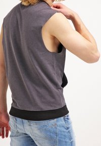 Camiseta sin mangas gris con un dobladillo negro, hecha de tela suave. El diseño presenta un escote redondo y un corte holgado.