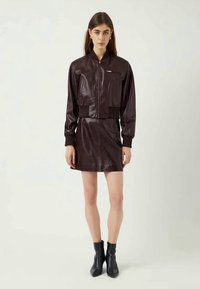 Burgundy leather dress with a zip front, fitted waist, and ribbed hem. Features long sleeves and a sleek design, paired with black ankle boots.