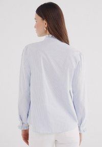 Lyseblå stribet bluse med lange ærmer, rynkede manchetter og en flæsekant, lavet af et glat stof for et poleret udseende.