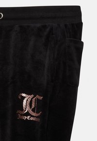 Os calções de veludo negro apresentam uma cintura com efeito canelado, bolso lateral e um logótipo metálico em rosa dourado "Juicy Couture" na perna esquerda.