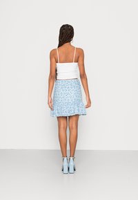 Haut blanc ajusté à fines bretelles, associé à une jupe évasée à motifs floraux bleus. Accentué avec des chaussures à talons de couleur bleu clair.