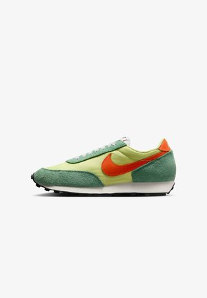 Niskoprofilowe buty sportowe z jasnoleśną tkaniną i panelami z zamszu, pomarańczowym logo Nike, białą środkową podeszwą i czarnym, wzorzystym spodem.