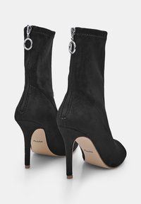 Juodi zomšiniai auliniai batai su aukštais stiletto kulnais, galiniais užtrauktukais su sidabriniais žiedais ir smėlio spalvos padais, pažymėtais "Bata".