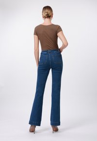 Blue high-waisted flared jeans with a dark wash, five pockets, and a cuffed hem, paired with a brown striped fitted top.