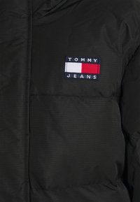 Giacca nera trapuntata con una toppa rettangolare del logo Tommy Jeans in bianco, blu navy e rosso sull'area sinistra del petto.