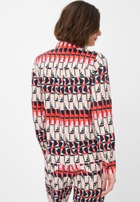 Blusa multicolore con un motivo geometrico in rosso, rosa, blu navy e crema. Caratterizzata da un colletto, chiusura a bottoni e maniche lunghe.