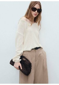 Light cream knitted sweater with an off-shoulder design, paired with high-waisted beige trousers and a dark brown woven handbag.