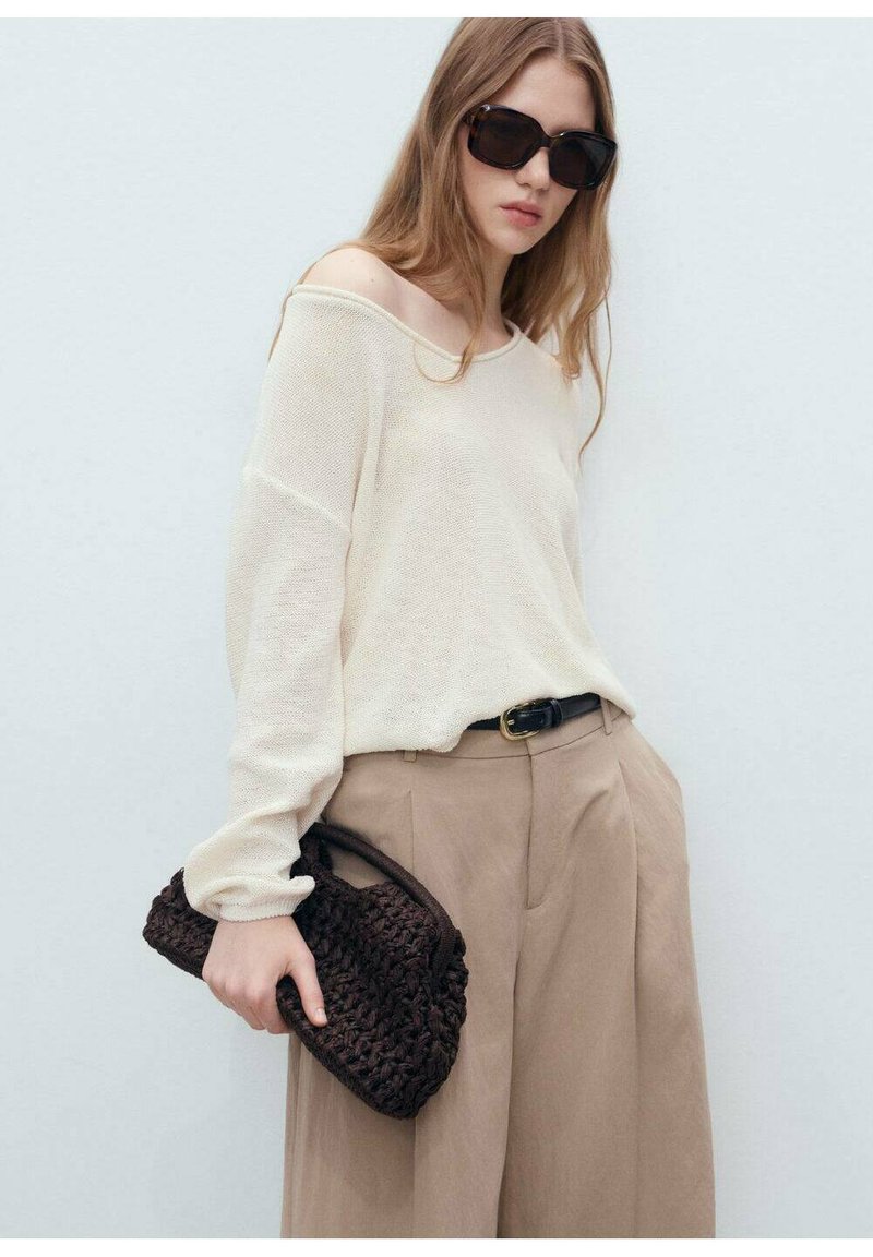 Light cream knitted sweater with an off-shoulder design, paired with high-waisted beige trousers and a dark brown woven handbag.