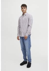 Camicia a righe con colori chiari e scuri, abbinata a jeans in denim blu chiaro e scarpe in suede nere. Presenta una tasca frontale.