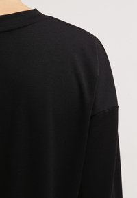 Maglietta nera a maniche lunghe con scollatura rotonda, caratterizzata da una texture liscia e una vestibilità comoda. Design minimale senza motivi o accenti visibili.