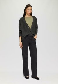 Ciemnoszary kardigan z guzikami, oliwkowa bluzka, czarne spodnie straight-leg i czarne buty. Gładka tekstura, minimalistyczny design.